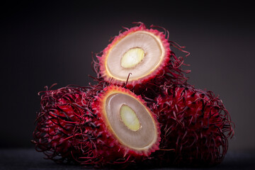 Lot of tropical exotic Rambutan fruit with typical vibrant red outer peel with spikes showing one...