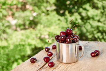 Metal mug with ripe red cherry on a green background of foliage.