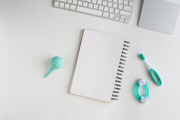 Keyboard, trackpad, notebook and baby utensils on white background suggesting working from home new mother of father