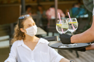 Woman with medical facemask and waiter with gloves keeping social distance in restaurant. Aftermath of covid-19 relief of Quarantine measures.