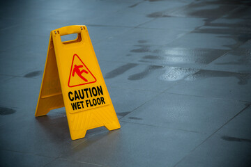 Yellow wet floor caution sign during rain with a puddle of water when the floor is slippery and...