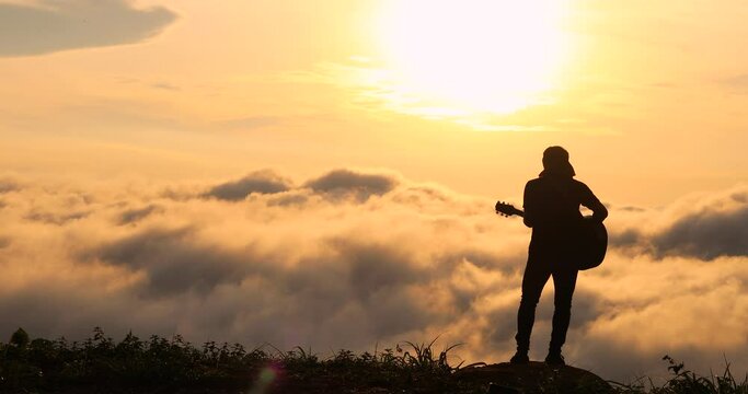 The silhouette of Musician playing guitar on sunset ,Music with sunrise or sunset ,guitar in nature,Foggy sky,Orange sky