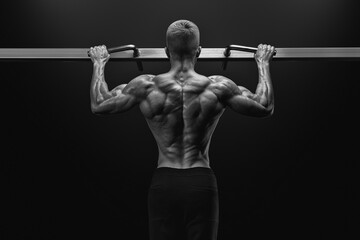 Black and white image of power muscular bodybuilder guy doing pullups in gym. Fitness man pumping up lats muscles. Fitness and bodybuilding training health lifestyle concept