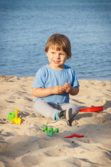 Smiling boy playing on sand at beach. Summer, vacation and relaxation time concept