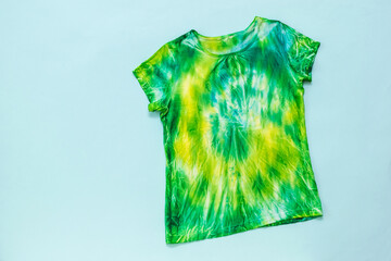 T-shirt in green, yellow and blue in tie dye style on a light blue background. Flat lay.