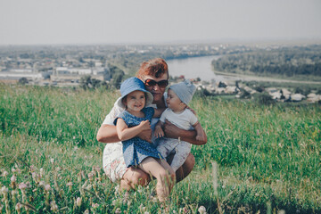 woman with babys walks in a meadow. Village houses, forest and river as background. The concept of summer, warmth, freedom, village life, sunburn, childhood