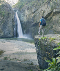 jimenoa waterfall landscape and man standing on top of rock rock with backpack from back rear...