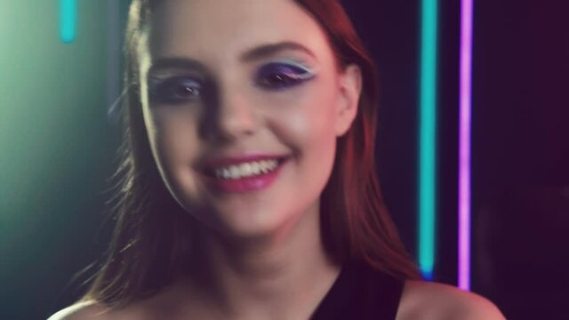 Fashion face. Glamour elegance. Cheerful girl with creative night makeup smiling in neon lights.