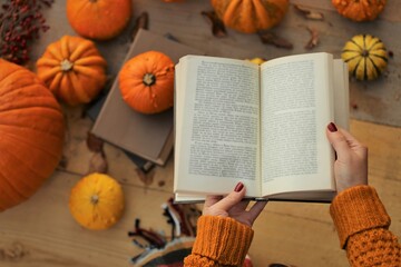 Autumn books.Learning and education concept.back to school. Halloween books. Open book  in female hands on  bright orange pumpkins background in bright sunshine.Cozy autumn mood . Fall season