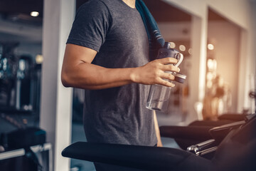 A man in running on treadmill at gym and holding bottle of water