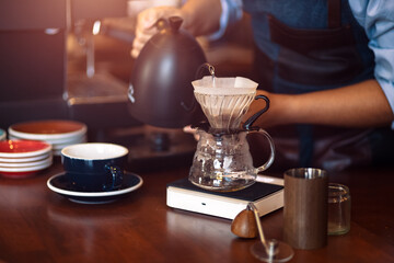 barista pouring boiling water from kettle to drip coffee maker.