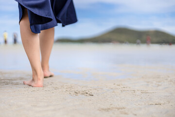 Woman barefoot walking on the beach at  summer along wave of sea water and sand.