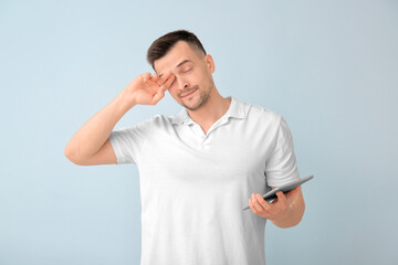 Tired man with tablet computer on color background. Concept of sleep deprivation