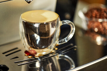 Espresso in a transparent cup, standing on a coffee machine with reflection. Freshly brewed coffee concept