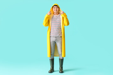 Young Asian man in raincoat on color background