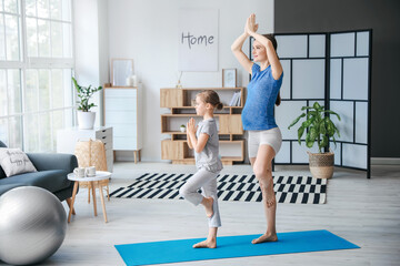 Young pregnant woman and her little daughter practicing yoga at home