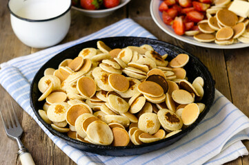 Heap of mini pancakes in a cast iron pan on wooden table