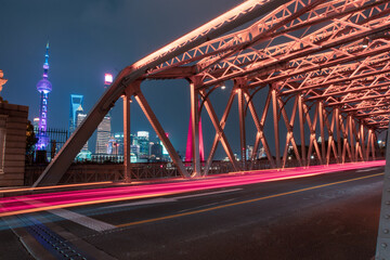night view of Waibaidu Bridge, a historic landmark in Shanghai, with traffic inside and skyscrapers in then back.