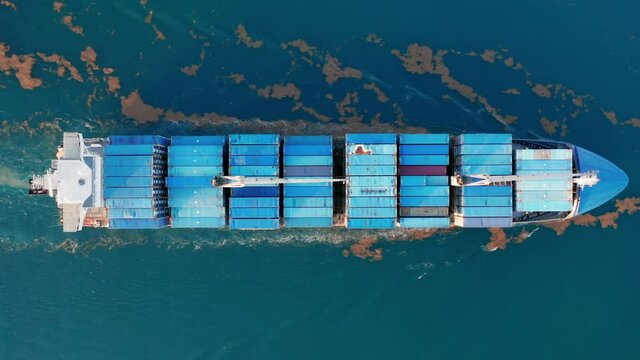 Top down 4K drone footage of water transportation. Aerial view of large container ship in Atlantic ocean. Big blue vessel stocked with cargo containers exporting goods. Massive freight shipment by sea