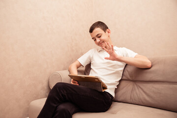 Teenager boy in white T-shirt sits on sofa with laptop