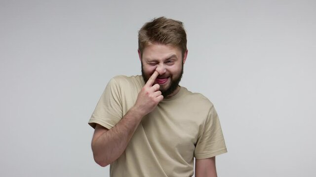 Funny crazy uncultured bearded man picking dirty nose, pulling out boogers and throwing disgusting mucus at camera, bad manners, ugly misconduct concept. indoor studio shot isolated on gray background