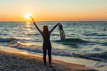 Silhouette of a girl in a wetsuit with flippers and a snorkel in her hands © Oleksandr