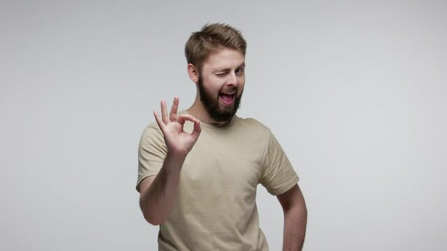 Okay, alright! Happy handsome bearded guy looking at camera with ok gesture and winking conspiratorially, completely agree and support some crazy idea. indoor studio shot isolated on gray background