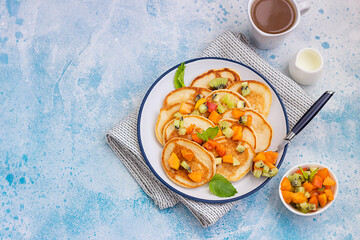 Homemade classic american pancakes with fruit salad made from apricot and kiwi. Healthy summer breakfast. Blue stone background. Top view. Copy cpace.