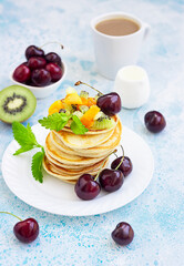 Breakfast with a cup of coffee and a stack of classic american pancakes served with black cherry, apricot, kiwi and mint. Blue stone background.