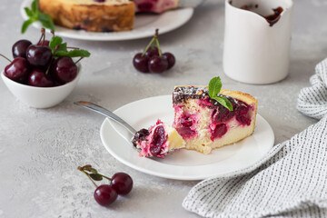 Cottage cheese casserole or no crust cheesecake with black cherry decorated with chocolate glaze, coconut flakes and mint on a light grey stone background.