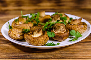 Plate with baked champignons, dill and parsley on a wooden table
