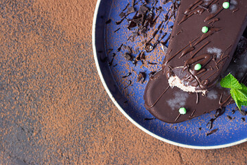 Ice cream popsicle covered with chocolate with mint on a blue ceramic plate. Dark textured background. Top view.