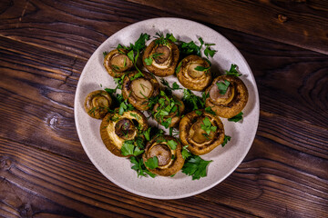 Plate with baked champignons, dill and parsley on a wooden table. Top view