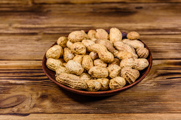 Ceramic plate with heap of unpeeled peanuts on wooden table
