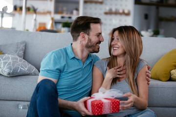  Husband surprising his wife with a gift. Young man giving a gift box to his wife.