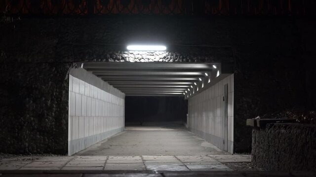 Man with backpack walking through the pedestrian underpass tunnel passage at night.