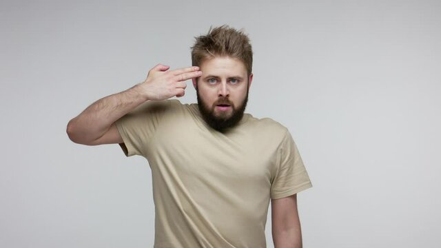 Insecure depressed frustrated guy doing suicide gesture, killing himself, shooting finger gun to head but weapon misfired, second chance to live. indoor studio shot isolated on gray background