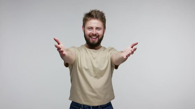 Come here into my arms! Cheerful optimistic bearded guy stretching hands, looking at camera with amiable friendly smile, going to embrace, share love. indoor studio shot isolated on gray background