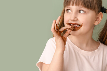 Cute funny girl with chocolate on her face and hands against color background