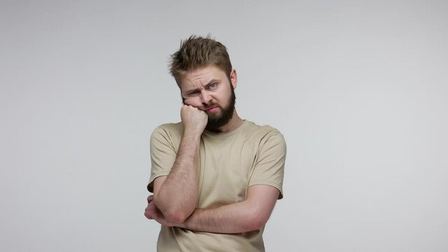 Bored unhappy man looking at camera indifferent gloomy depressed, leaning on hand listening boring talk, apathetic emotions, laziness and lack of energy. indoor studio shot isolated on gray background
