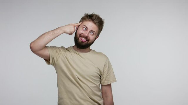 I am idiot! Funny bearded man gesturing finger against temple doing stupid gesture, looking at camera with dumb brainless silly expression, cuckoo out of mind. studio shot isolated on gray background