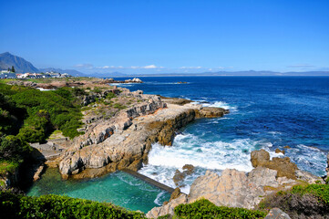 Beautiful Atlantic Ocean coast in Hermanus with waves crashing on the shore and houses on the cliff on sunny day, South Africa