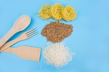 Fototapeta na wymiar buckwheat, rice, raw pasta and wooden cutlery on a blue background. View from above.