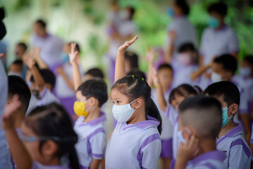 Obraz premium Young Asian girls in kindergarten, schools in Thailand wear protective masks. The Covid-19 Virus Stand in line and social distancing, stand in line, prepare to attend school