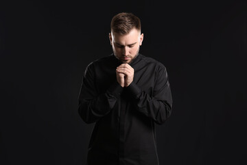 Young priest praying to God on dark background