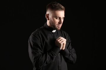 Fototapeta premium Young priest praying to God on dark background