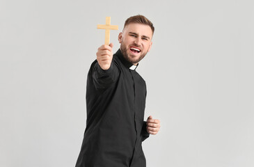 Emotional young priest with cross on light background