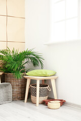 Stool with wicker baskets, pillow and houseplant in room