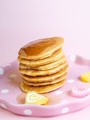 Pouring honey syrub on pancake stack on pink background.