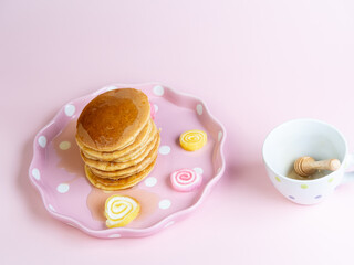 Pouring honey syrub on pancake stack on pink background.